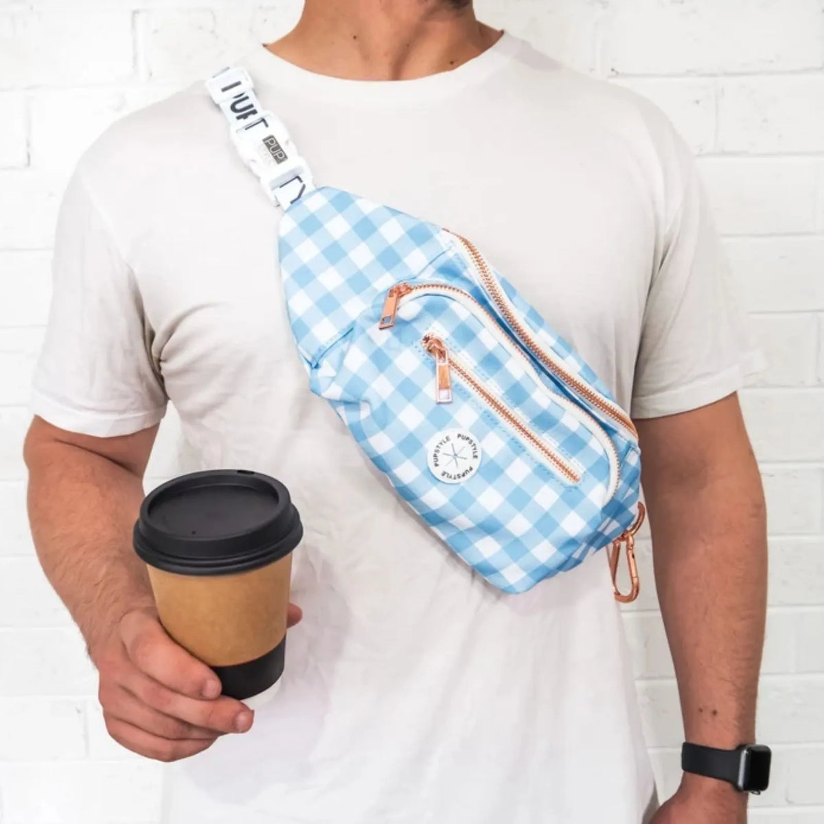 A man wearing a white t-shirt and holding a coffee cup, wearing a Pupstyle Blueberry Muffin Dog Parent Bum Bag across his chest. The bag has a white adjustable strap with black text and rose gold zipper pulls.