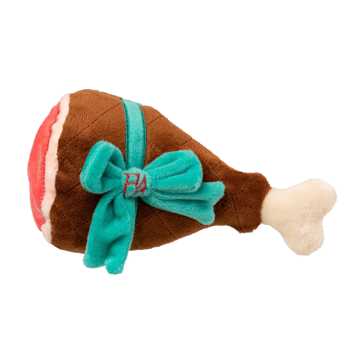A FuzzYard Christmas Humble Holiday Ham plush dog toy, with a brown body, cream-colored bone at the end, red and white striped detailing on the head, and a teal bow tied around the middle.