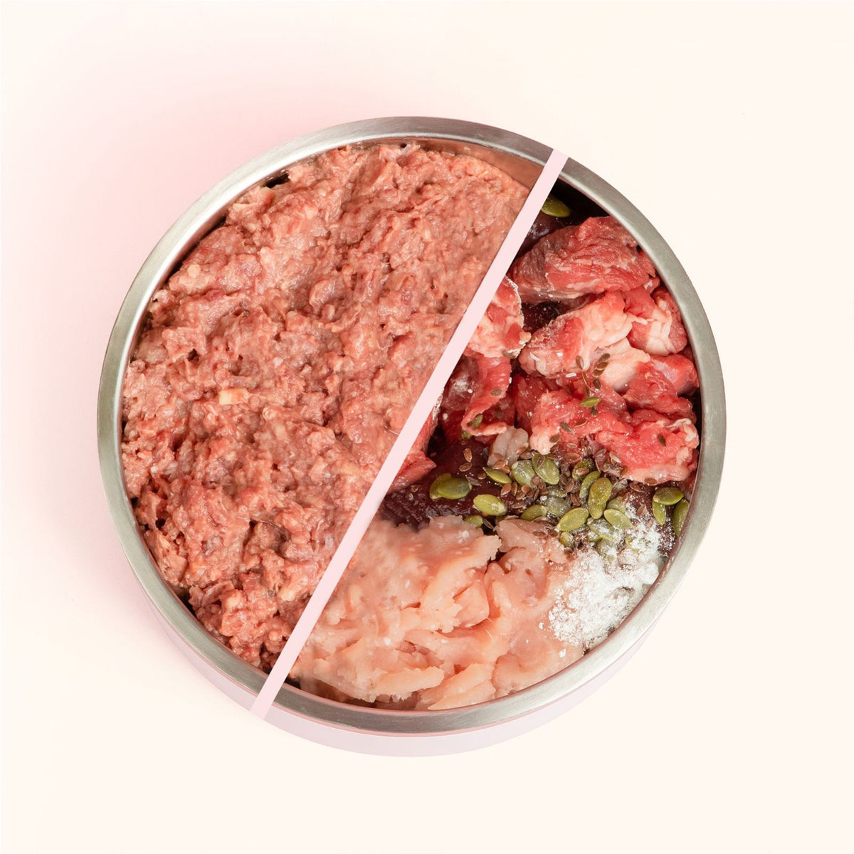 A top-down view of a round metal Turkey and Chicken Cat food bowl filled with split ingredients: raw ground meat on the left, raw sliced meat on the right, plus visible pumpkin seeds, white powder, and a pale pinkish chunk on a light pink background.