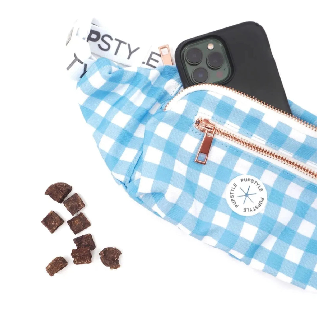 A Pupstyle Blueberry Muffin Dog Parent Bum Bag with a rose gold zipper, shown with a black smartphone inside and a few dog chew pieces on a white background. The brand 'Pupstyle' is visible on the strap and the circular patch on the front.
